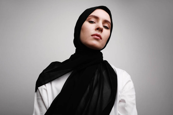 Portrait of young beautiful muslim woman in hijab. Isolated over white wall. Space for text. - 写真・画像