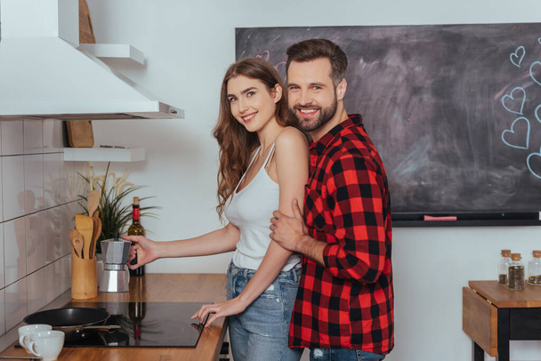happy young couple smiling at camera while making coffee in geyser coffee maker - Foto, Imagen