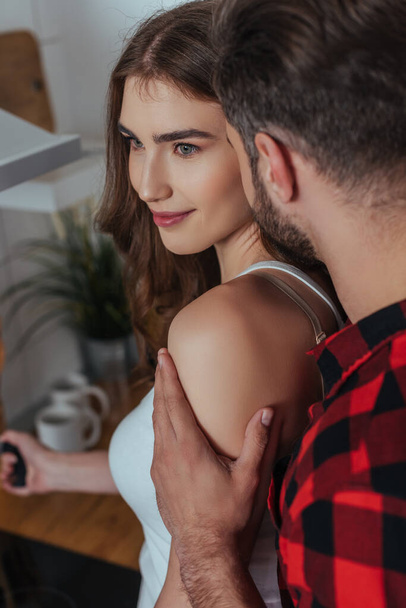 young man touching shoulder of attractive girlfriend in kitchen - Fotó, kép