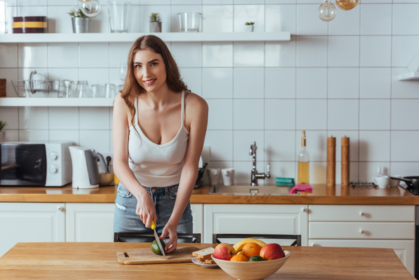 happy, beautiful girl smiling at camera while preparing breakfast with fresh fruits - Fotografie, Obrázek
