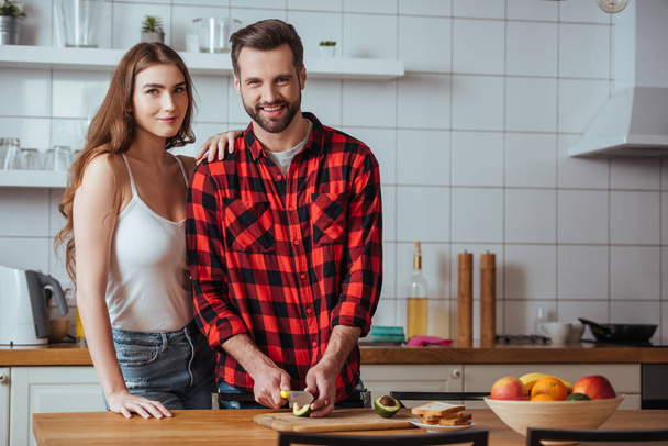 happy young couple smiling at camera while preparing breakfast with fresh fruits together - Foto, imagen