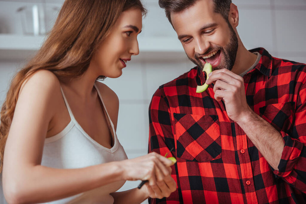 cheerful man tasting slice of fresh avocado near attractive girlfriend - Foto, afbeelding