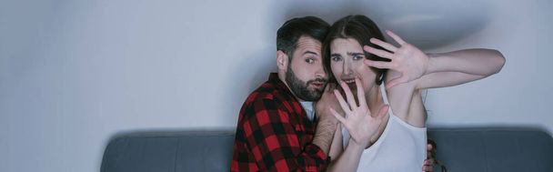 scared girl with outstretched hands watching movie near frightened boyfriend, horizontal image - Photo, Image