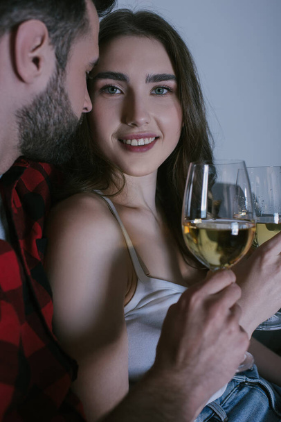 happy girl smiling at camera while sitting near boyfriend with glasses of white wine - Foto, Imagem