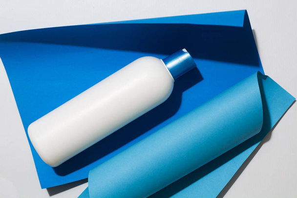 Frasco de plástico branco, recipiente para shampoo e cosméticos líquidos em fundo azul brilhante
. - Foto, Imagem