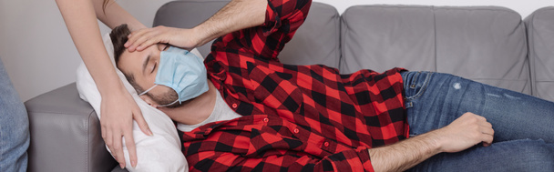cropped view of woman touching pillow while sick boyfriend lying on sofa and holding hand on head - Foto, afbeelding