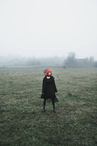 Menina da moda com corte de cabelo bob vermelho e roupas pretas no campo de outono nebuloso frio dramático
 - Foto, Imagem