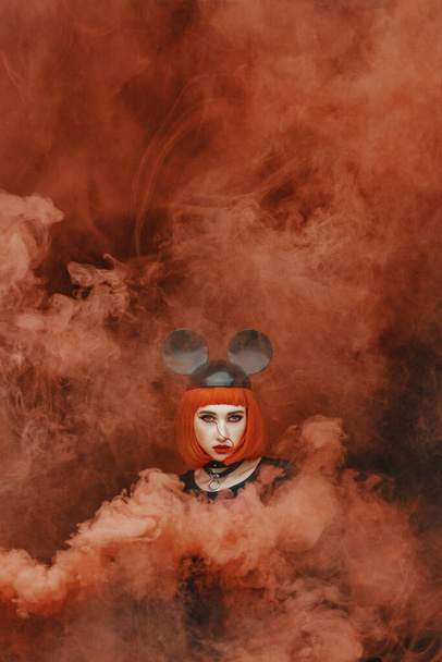 Portrait de jolie fille de la mode avec bob rouge coupe de cheveux et chapeau de souris dans la fumée rouge épaisse, jeune femme avec chapeau de souris et bombe de fumée avec fond sombre
 - Photo, image
