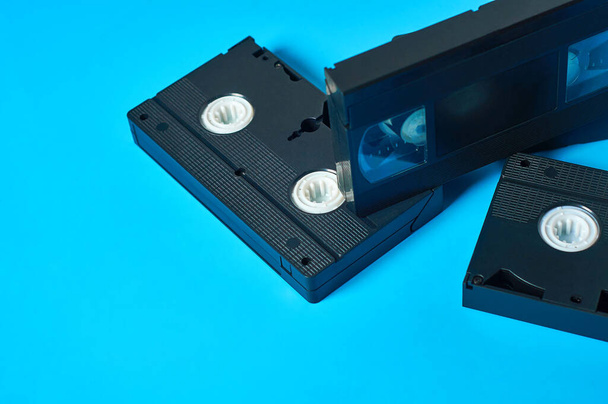 Scattered black old plastic vhs video cassettes lies on blue desk. Concept of 90s. Copy space - Zdjęcie, obraz