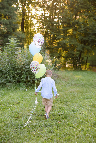 Хлопчик початкового шкільного віку біжить з повітряними кульками. Хлопець вказує спину до камери
. - Фото, зображення