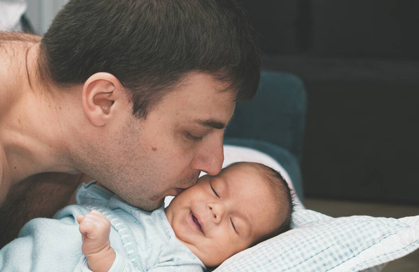 Egy gondoskodó apa megfogja és megcsókolja a babát. Boldog család otthon.. - Fotó, kép