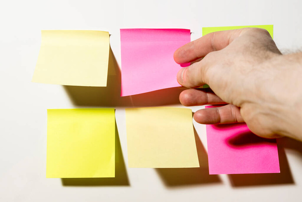 A hand shoots multi-Colored square post-it notes pasted on a white wall in the office - Фото, зображення