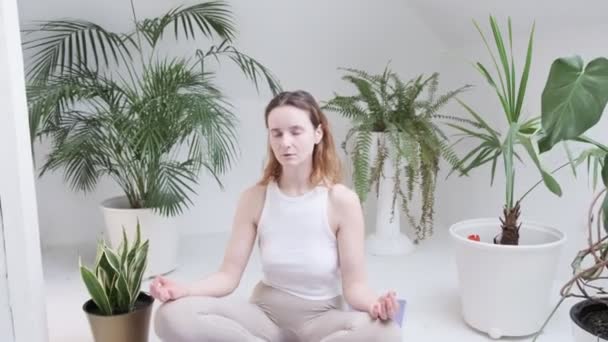 girl wearing sportswear sits in lotus pose with closed eyes enjoys meditation - Footage, Video