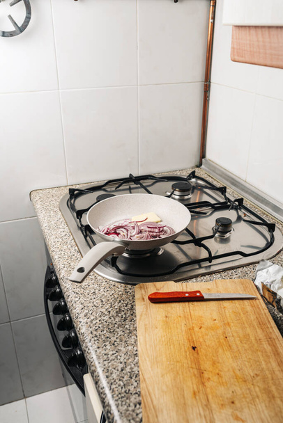 сковорідка з подрібненою червоною цибулею та маслом на кухонному вогні
 - Фото, зображення