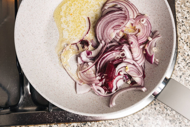 sartén con cebolla roja picada y mantequilla en el fuego de la cocina
 - Foto, Imagen