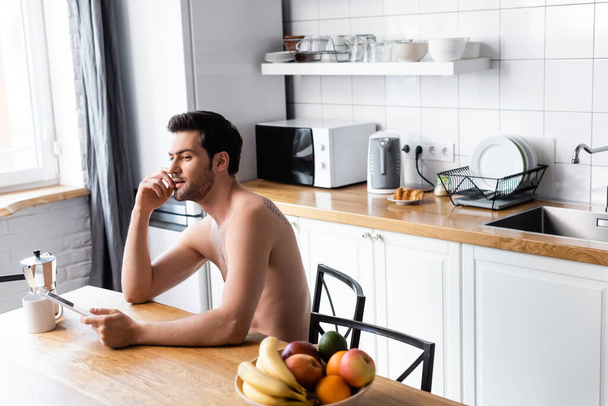 Mutfakta meyve ve kahveyle dijital tablet kullanan seksi tişörtsüz bir adam.  - Fotoğraf, Görsel