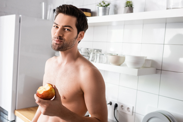 shirtless man eating apple on kitchen in morning - Foto, Imagem
