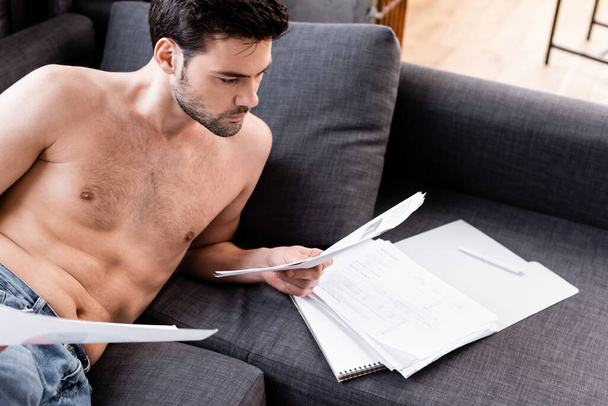 shirtless male freelancer doing paperwork on sofa during quarantine - Foto, imagen