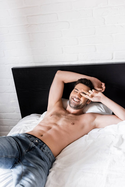handsome shirtless smiling man relaxing on bed at home - Фото, изображение