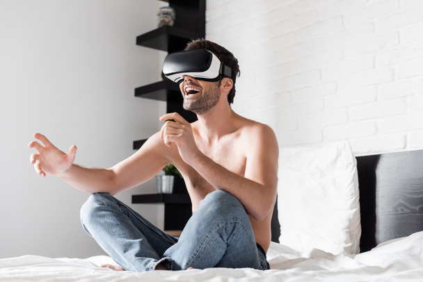 izgatott félmeztelen férfi gesztikulál használata közben virtuális valóság headset az ágyban - Fotó, kép