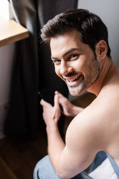 uomo senza camicia sorridente utilizzando smartphone con schermo bianco a casa
 - Foto, immagini