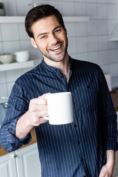 Χαρούμενος όμορφος άντρας που κρατάει καφέ στο σπίτι σε καραντίνα. - Φωτογραφία, εικόνα