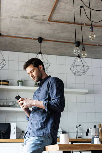 молодий чоловік використовує смартфон на кухні з кавою під час карантину
   - Фото, зображення