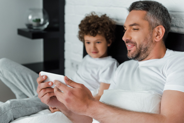 selective focus of bearded father holding smartphone near son  - Photo, Image