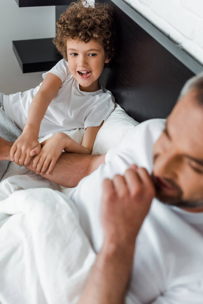 selective focus of curly kid looking at happy father in bedroom  - Photo, Image