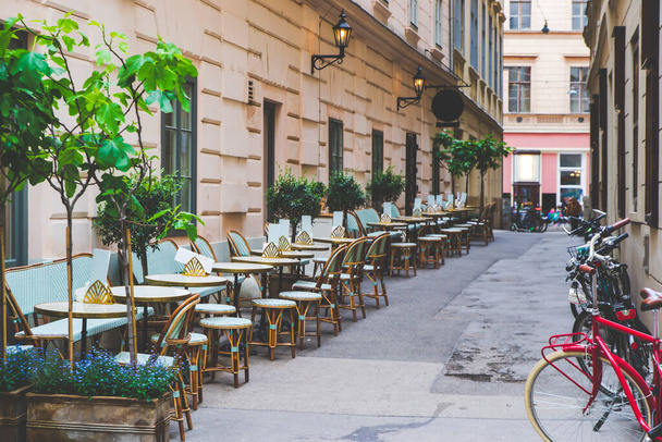 Küçük caddede, sol tarafta kahverengi sandalyeli yeşil sandalyeler ayakta duran bisikletlerdir. Avusturya, Viyana 'da turistik yol. Avrupa şehir manzarası gibi eski dar sokaklar.  - Fotoğraf, Görsel