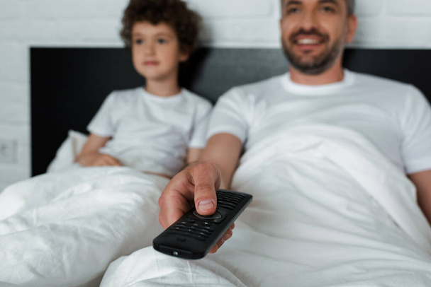 selective focus of cheerful man holding remote controller near son  - Fotografie, Obrázek