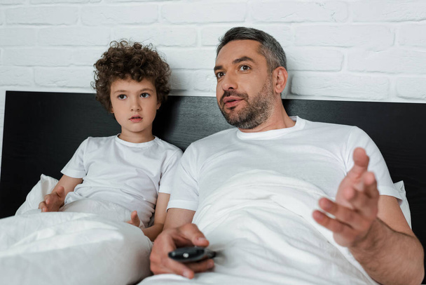 selective focus of father gesturing while holding remote controller near curly son  - 写真・画像