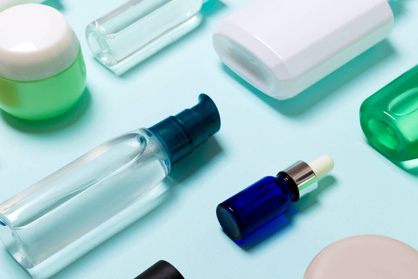 Top uitzicht van cosmetische producten in verschillende potten en flessen op blauwe achtergrond. Close-up van containers met Kopieer ruimte. - Foto, afbeelding