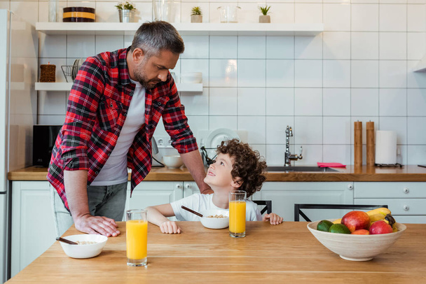 cheerful boy looking at handsome father near breakfast on table  - Photo, Image
