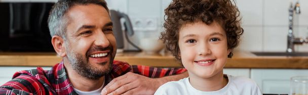 panoramic crop of cheerful father looking at smiling and curly son  - Fotoğraf, Görsel