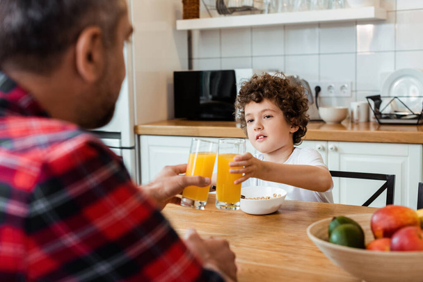 selective focus of father and son clinking glasses of orange juice  - Foto, Bild
