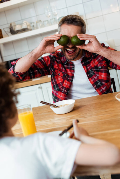 selective focus of father covering eyes with ripe avocados near curly boy  - Foto, Imagem