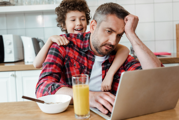 focalizzazione selettiva di figlio felice toccando padre freelance stanco che lavora da casa
 - Foto, immagini