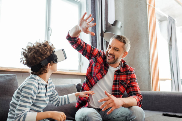 gelukkig vader geven high vijf naar krullend zoon in virtual reality headset  - Foto, afbeelding