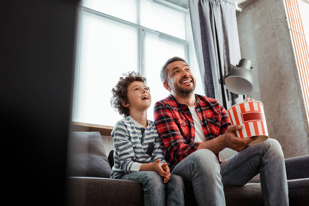 selective focus of cheerful and curly kid watching movie near father holding popcorn bucket  - Фото, зображення