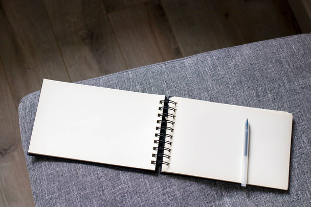 Um caderno branco aberto com molas encontra-se em um sofá cinza. Espaço para texto
 - Foto, Imagem