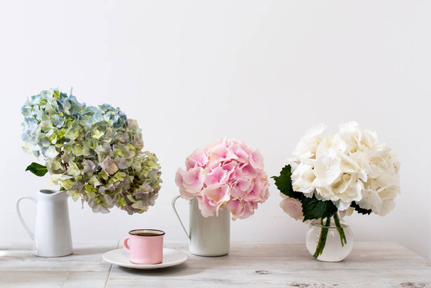 A large branch with green and blue and pink pastel hydrangea in a white jug on a beige table. Copy space - Fotó, kép