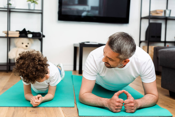 bebaarde vader en gekrulde zoon oefenen op fitness matten  - Foto, afbeelding
