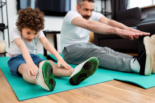 selective focus of curly son and father exercising on fitness mats  - Fotografie, Obrázek