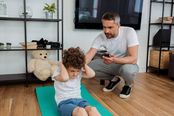 handsome father counting while curly son exercising on fitness mat  - Фото, зображення