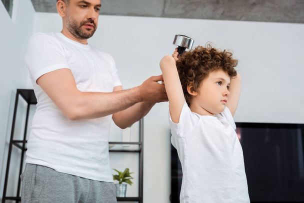 przystojny ojciec dotykając hantle podczas kręcone syn ćwiczenia w domu - Zdjęcie, obraz
