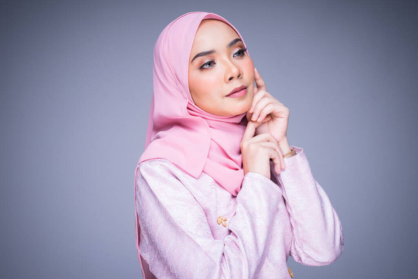 Headshot portret van een mooi vrouwelijk model met traditionele kleding en hijab, een lifestyle kleding voor moslimvrouwen geïsoleerd op grijze achtergrond. Idul Fitri en hijab modeconcept. - Foto, afbeelding