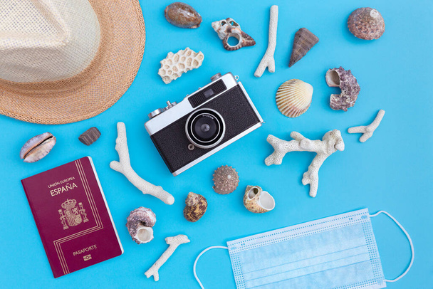 青の背景に藁帽子、保護顔マスク、パスポート、アナログ写真カメラとビーチシェルのトップビュー。コロナウイルスcovid-19 、夏休みと旅行のコンセプト. - 写真・画像