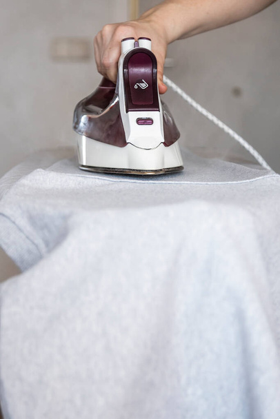 αγνώριστη γυναίκα σιδέρωμα ρούχα στην σιδερώστρα στο σπίτι - Φωτογραφία, εικόνα