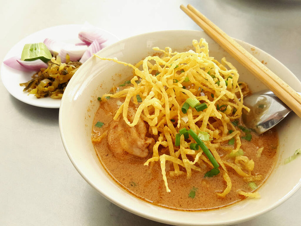 El nombre de los alimentos tailandeses es khao soi, vista de cerca de los fideos de curry con sopa de leche de coco en un tazón con guarnición es verduras en vinagre en la mesa
.  - Foto, Imagen